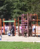 Children play in a park playground surrounded by trees and open space