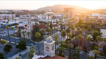 Aerial view of downtown Riverside, California, with Mission Inn towers, palm trees, streets, and mountains at sunset.