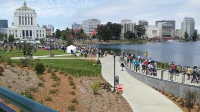 Crowd gathered along a lakeside park with city skyline and a domed civic building in the background.
